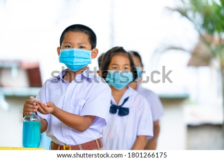Asia elementary children spraying classmate's hands with disinfectant while wearing protective face masks on a class in the classroom. 