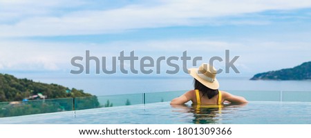 Summer travel vacation concept, Happy traveler asian woman with hat and bikini relax in luxury infinity pool hotel resort with sea beach background at day in Phuket, Thailand