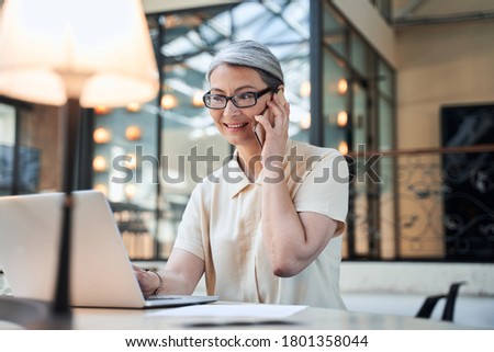 Successful businesswoman looking at her laptop screen while having a phone call in her office