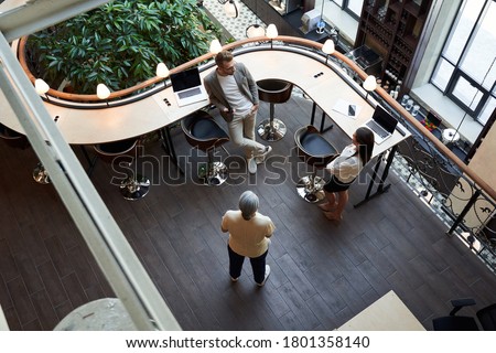 Top-view of handsome young man and beautiful young woman talking to a senior woman in a coworking space