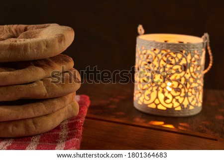 several pita breads stacked on a rustic cloth and a cutting board on a wooden table with black background