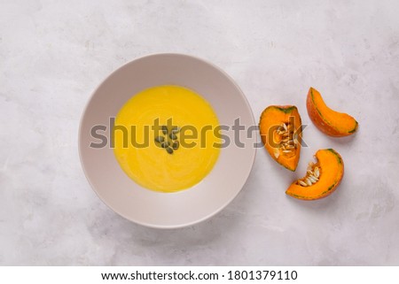 Pumpkin puree soup in a plate on a light background. Pumpkin slices, healthy food, farm products
