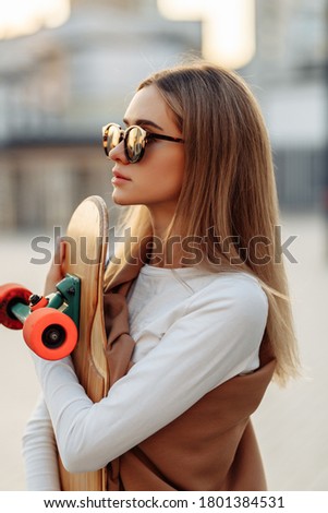 Woman in glasses with a skate in her hands. Longboarding around the city. High quality photo