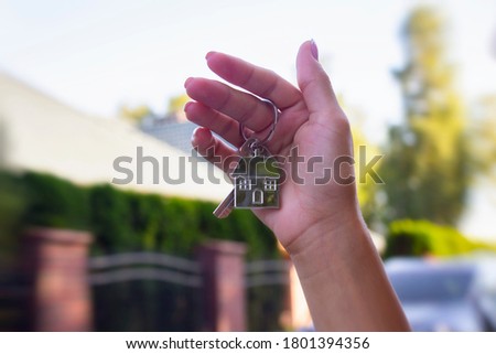 A woman holds in her hands the keys to the house against the background of residential buildings. Concept for buying and renting apartments