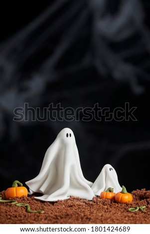 Scene of halloween, ghost couple, parent and son, surrounded by pumpkins made of sugar paste on chocolate cake ground, black background, copy space