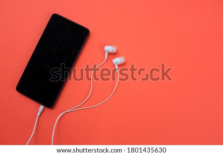 The phone is plugged in white headphones on an orange background