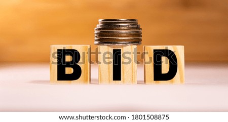The concept of the word bid on wooden cubes with coins on a white wooden background. Business concept.
