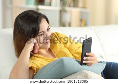 Woman watching media on smartphone lying on a sofa in the living room at home