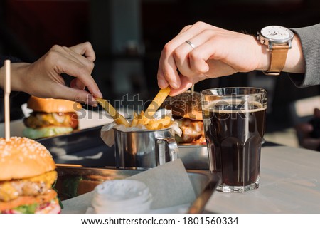 Friends eating French fries, burgers and drink cold dark beer. 