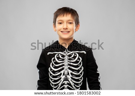 halloween, holiday and childhood concept - smiling boy in black costume of skeleton over grey background