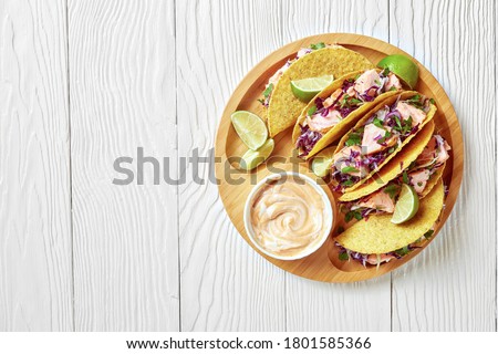 salmon tacos with red cabbage salad with spicy yogurt sauce sprinkled with finely chopped parsley served on a bamboo plate on a white wooden table, horizontal view from above, flat lay, free space