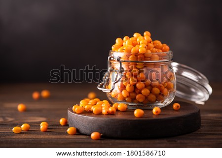 ripe sea buckthorn berries in a glass jar on wooden board Royalty-Free Stock Photo #1801586710