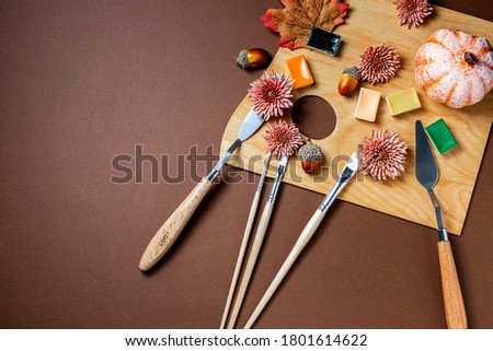 Autumn still life with professional art materials, artist's palette, paints, brushes, acorns, autumn leaves on wooden background. Autumn concept. The workplace of the artist. Flat lay, top view