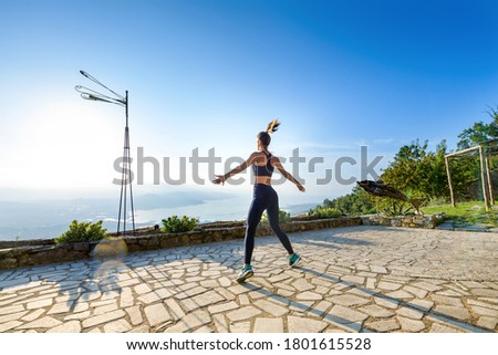 Young woman doing a morning exercise workout at sunrise in a wide angle view outdoors in the garden on a paved patio in a health and fitness concept