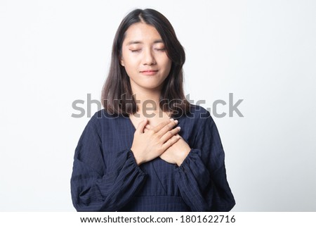 Faithful woman closes eyes and keeps hands on chest near heart, shows her kindness on white background