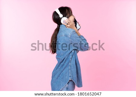 Side view Young Asian woman wearing headphones dancing and listening to music from smartphone shoot in isolated on pink background