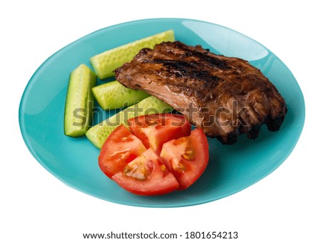 grilled pork ribs with sliced cucumbers and tomatoes on turquoise plate. pork ribs isolated on white background. ribs grill top side view