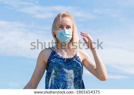 Healthcare and medicine concept. Portrait of blonde woman with windswept hair and medicine mask on her face. Woman wear blue dress in blue sky background with copy space