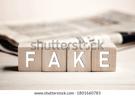 The word fake on wooden blocks with a newspaper background. Fake news in media concept.  Royalty-Free Stock Photo #1801660783