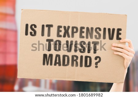 The question " Is it expensive to visit Madrid? " on a banner in men's hand with blurred background.  