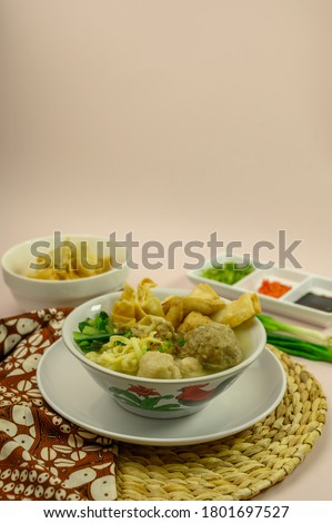 top view of Indonesian food named bakso malang or bakwan malang (meatball soup) completed with noodles, green cabbage, fried soybean cake, fried dumplings and sambal isolated on pink background