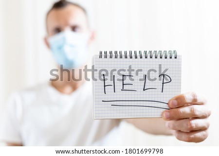 a man in a medical mask shows a sheet of paper with the inscription HELP