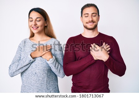 Beautiful couple wearing casual clothes smiling with hands on chest with closed eyes and grateful gesture on face. health concept. 