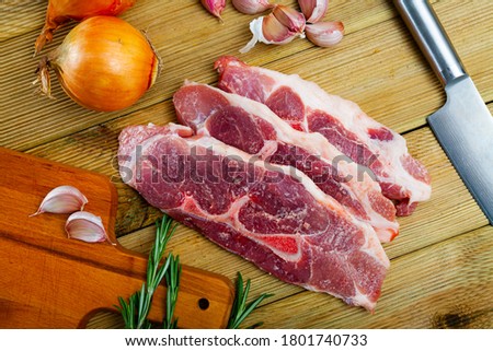 Raw pork's fillet shoulder with rosemary and garlic on wooden surface, nobody