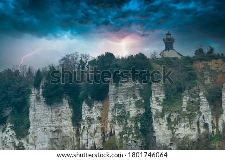 Lighthouse on a chalk cliff under a dramatic thunderstorm sky in Normandy, France