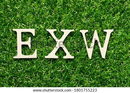 Wood alphabet letter in word EXW (abbreviation of Ex works) on green grass background