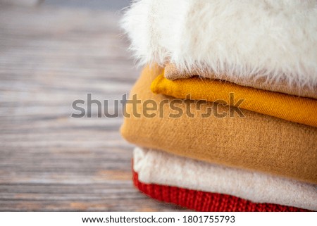 Pile of knitted woolen sweaters autumn colors on wooden table. Clothes with different knitting patterns folded in stack. Warm cozy winter fall knitwear concept. Copy space.