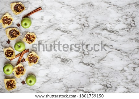Mini apple pies with phyllo crust with fresh fruit, star of anise and cinnamon bark over a white and black marble background. Top view or flatlay.