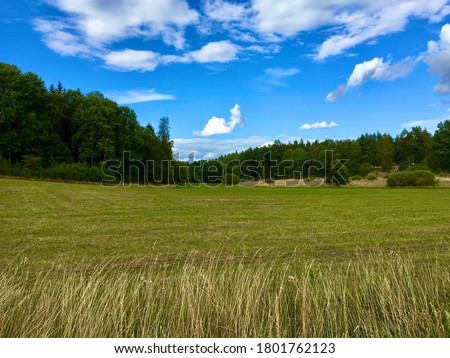 A beautiful view over a great field or landscape. A green forest in the rear och the picture. Clear blue sky with plenty of clouds. Nice climate and weather this sunny day. Jarfalla, Stockholm, Sweden
