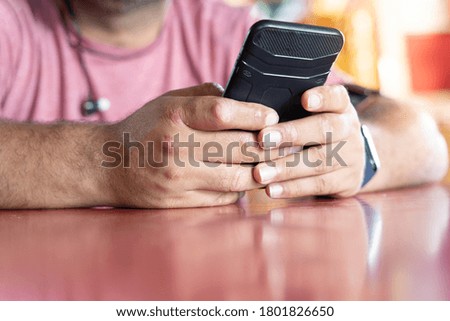 A man's hands using a mobile phone sitting at a table