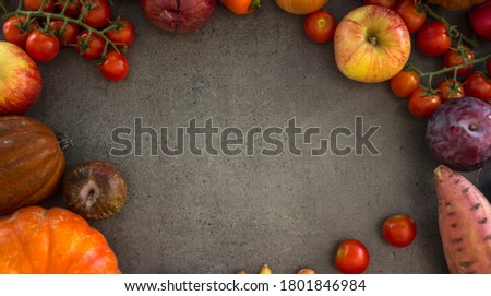 Top view photo of pumpkins, carrots, apples, cherry tomatoes and red onion on grey background with copy space. Colorful frame or border made of fresh autumn vegetables. 
