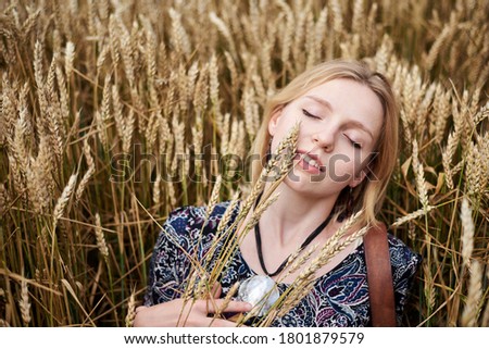 Young blond woman, wearing boho hippie clothes, lying, resting on wheat stalks in the middle of field. Close-up picture of beautiful female face on natural background. Eco tourism. Creative portrait.