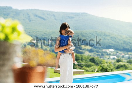 Young mother holding small daughter outdoors in backyard garden.