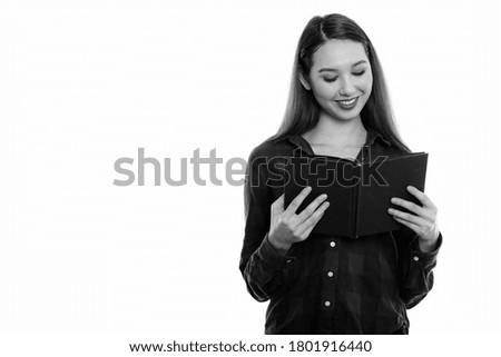 Studio shot of young happy beautiful Asian woman smiling while reading book