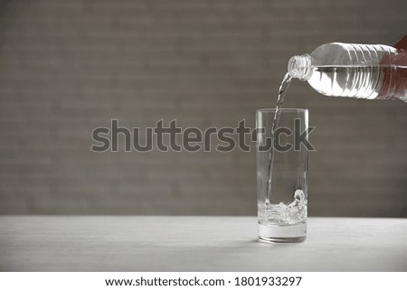 Pouring water from bottle into glass on table against blurred background. Space for text