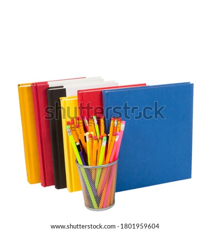 Vertical shot of a group of colorful books standing up with a wire pencil holder in front full of pencils.  White background.  Copy space.