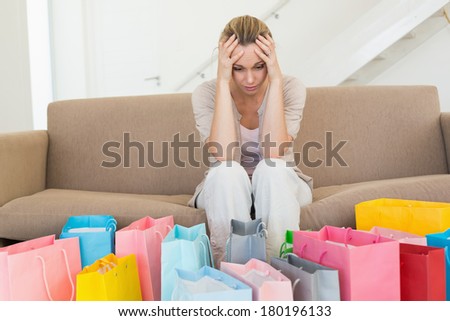 Regretful woman looking at many shopping bags on the couch at home in the living room Royalty-Free Stock Photo #180196133