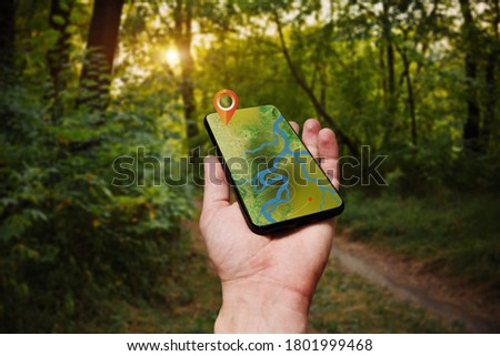 Navigation map with forest terrain and river on smartphone display. Concept of tourism and orienteering. Man hand hold in hand phone with use on-line maps  Royalty-Free Stock Photo #1801999468