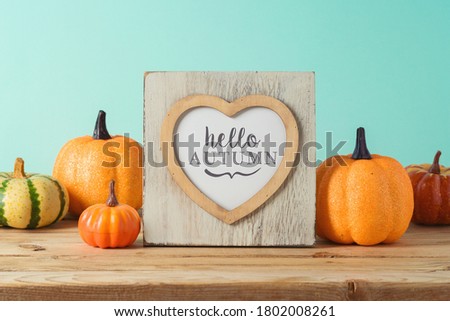 Hello Autumn concept with heart shape photo frame and pumpkin decor on wooden table over blue background. 