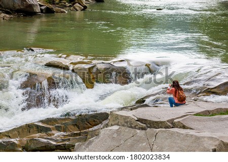 A woman takes a picture of a waterfall on a mountain river.