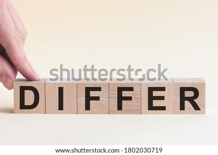 DIFFERENT message word on a wooden desk on cube blocks. The hand puts a wooden cube with the letter D from the word DIFFER. The word is written on cubes standing on the yellow surface of the table.
