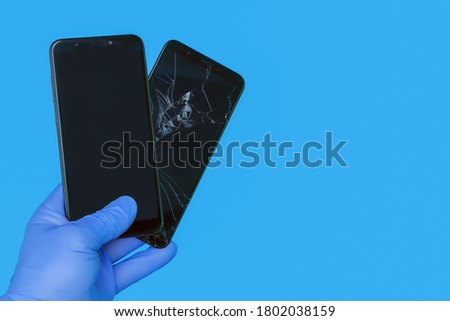 gloved hand holds new smartphone replacing an old broken smartphone with a cracked screen on a blue background, the concept of a quality smartphone repair service, place for copyspace