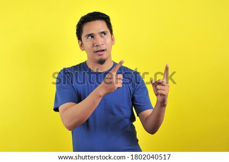 Friendly-looking lively pleasant Asian male with white t-shirt smiling delighted look at copy space joyful. Self-assured pointing
