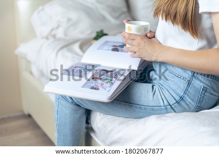 Cropped woman hands holding coffee and watching a family photo album. Mother sit on bed and watching album with little baby son kid boy.