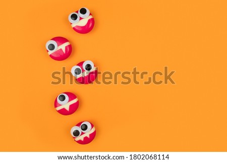 Cheese in form of little monsters with eyes on orange backdrop. Halloween decor for party. Space for text. Food art