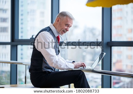 Adult male businessman, teacher, mentor working on a new project. Sits by a large window on the table. He looks at the laptop screen.